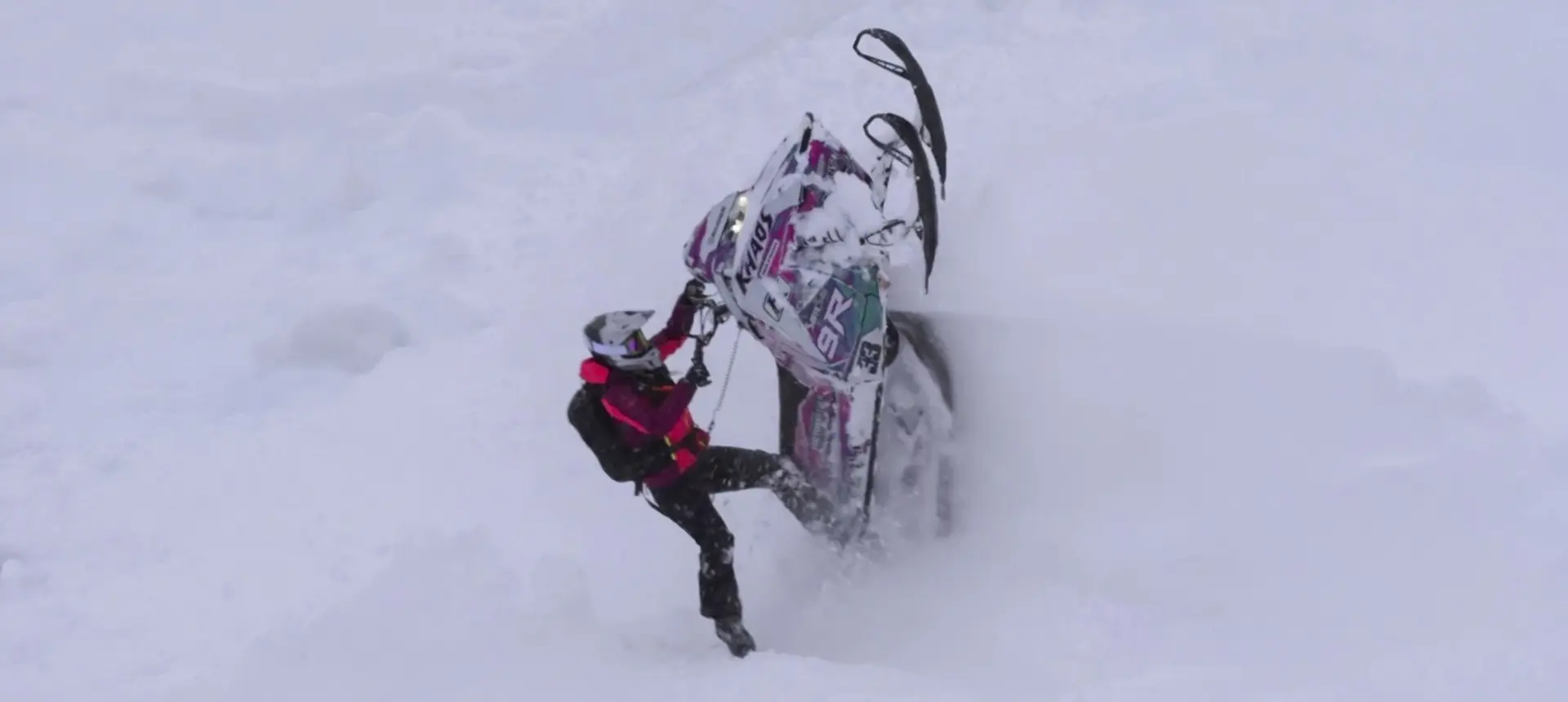 Mikaela Grönlund maneuvering a custom Polaris RMK Khaos snowmobile through deep mountain snow.