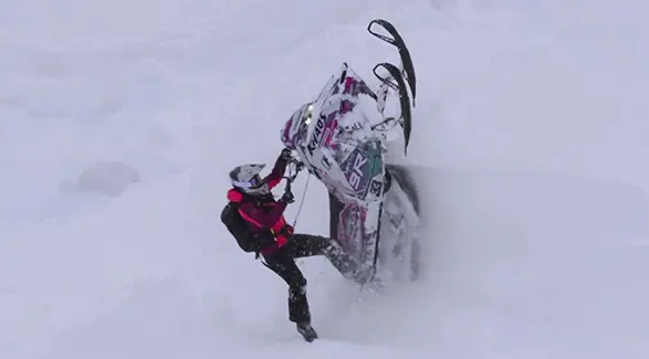 Mikaela Grönlund maneuvering a custom Polaris RMK Khaos snowmobile through deep mountain snow.
