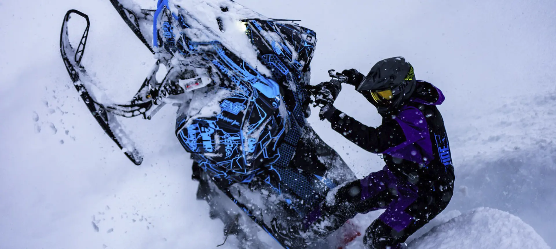 Ty Desrochers maneuvering a custom blue Polaris snowmobile through deep powder.