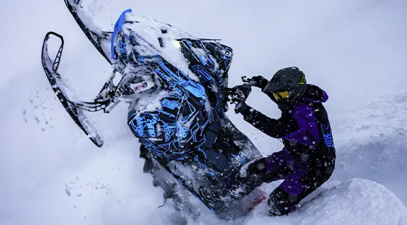 Ty Desrochers maneuvering a custom blue Polaris snowmobile through deep powder.