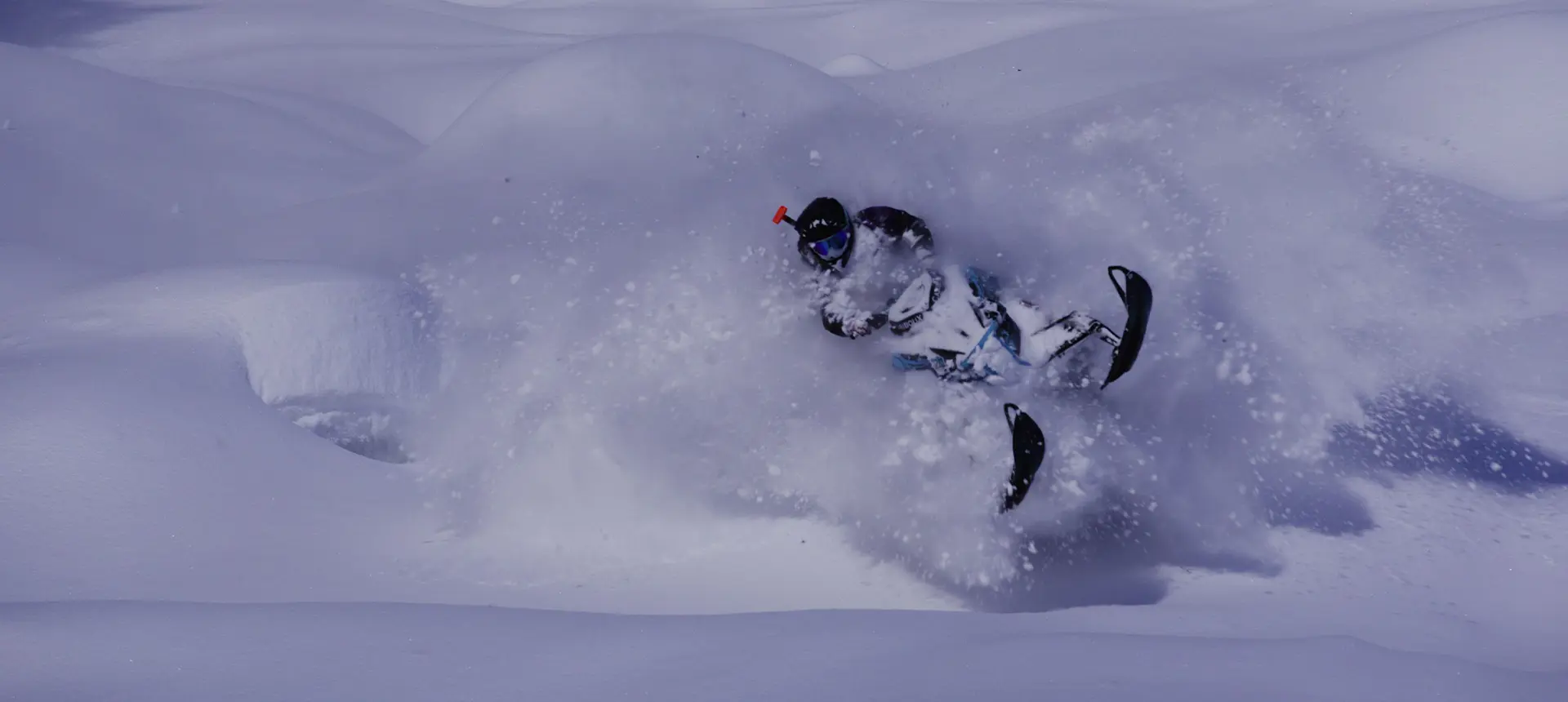 Ty Desrochers carving a Polaris snowmobile through deep mountain powder, spraying snow across the trail.