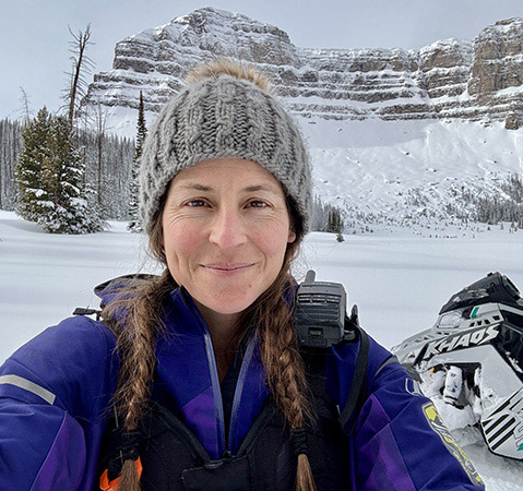 Mandy Fabel beside a Polaris RMK Khaos in a snowy mountain landscape with rugged cliffs.