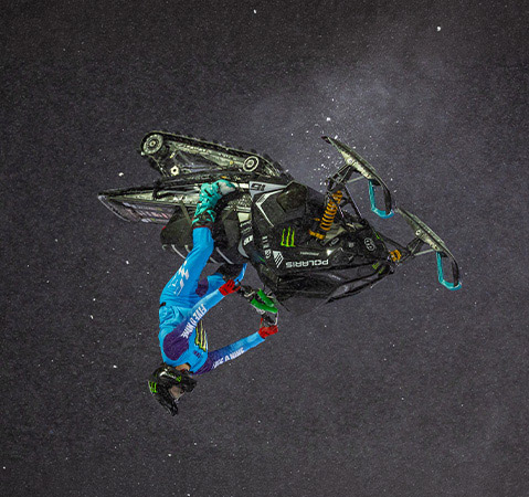Overhead view of Brett Turcotte performing an aerial stunt on a black Polaris snowmobile.