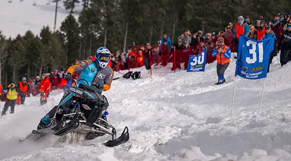 Helmeted rider racing a Polaris snowmobile through a groomed snow course lined with Polaris banners.