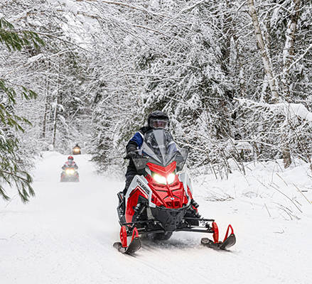 Rider on a 2-up 2027 INDY Adventure snowmobile showcasing the FOX® QS3 shocks.