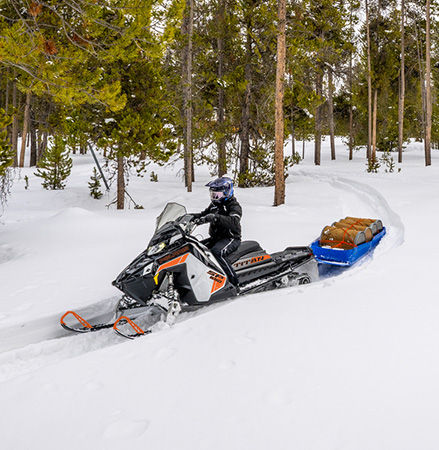 A rider on a 2027 Polaris TITAN SP widetrack snowmobile pulling a heavy sled.