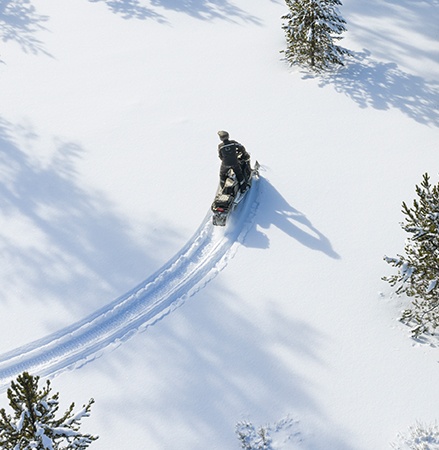 Rider cruising through the forest on a 2027 Polaris Voyageur Adventure sport-utility snowmobile.