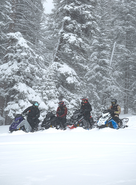 2 athletes from Team Polaris relaxing after a ride in the mountains with their Polaris snowmobiles. 