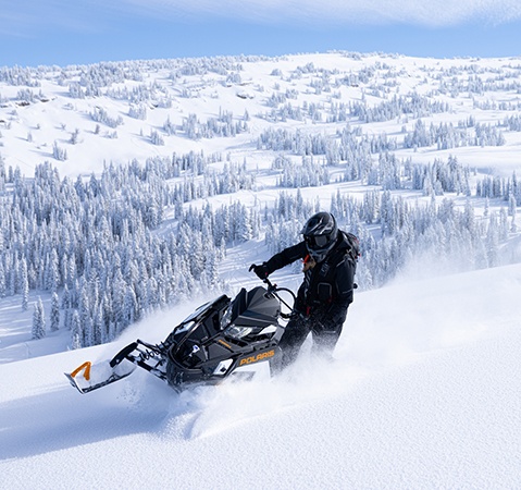 A rider cruising on a mountainside with a Polaris snowmobile featuring the 850 Patriot engine.