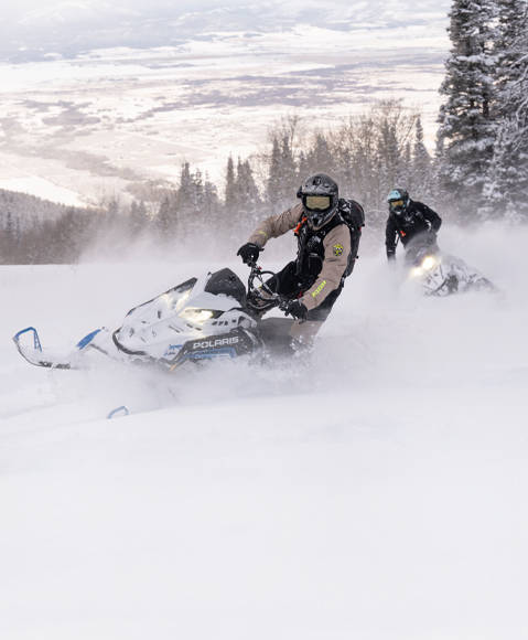Riders carving through a mountainside on a 2026 Polaris RMK mountain snowmobiles.
