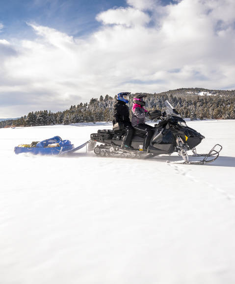 Rider cruising a trail on a 2026 Polaris Voyageur sport-utility snowmobile.