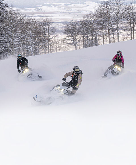 3 riders carving through a mountainside on 2027 Polaris RMK mountain snowmobiles.