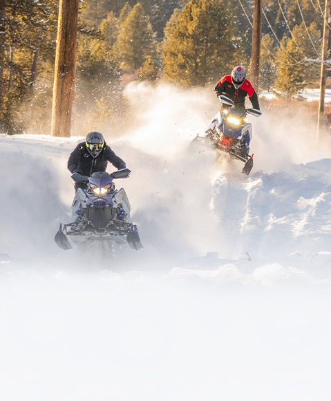 2 riders ripping off the beaten path on 2027 Polaris Switchback crossover snowmobiles.