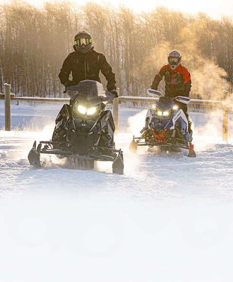 2 riders trail riding on their 2027 Polaris INDY trail snowmobiles.