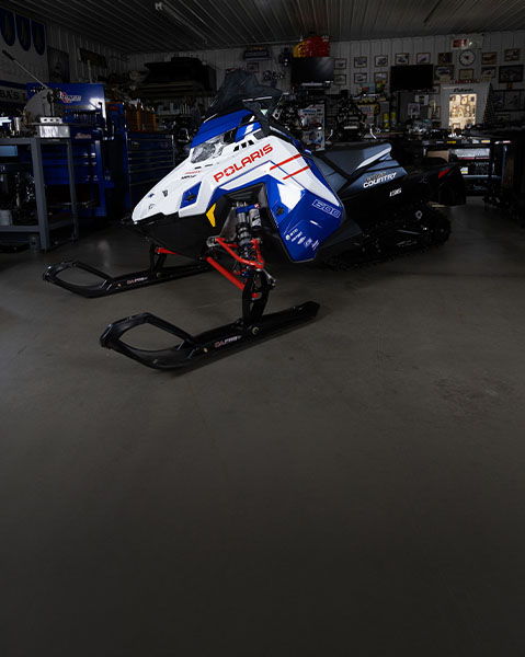 2027 Polaris 600 INDY Cross Country snowmobile displayed inside a workshop with blue, white and red bodywork.