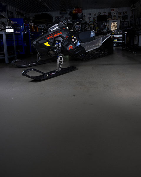 2027 Polaris 600R race snowmobile displayed inside a workshop with tools and equipment in the background.