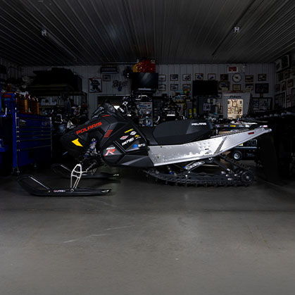 Side view of a black 2027 Polaris 600R race snowmobile displayed inside a workshop.