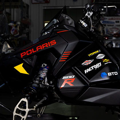 Close-up of the black 2027 Polaris 600R race snowmobile bodywork, front suspension and sponsor decals.