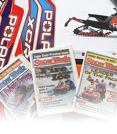 A collection of snowmobile-related items, including a colorful Polaris snowmobile poster, an Eagle River Preview Issue magazine titled ‘Snow Week,’ and another Snow Week magazine with the headline ‘Leader of the Pack.