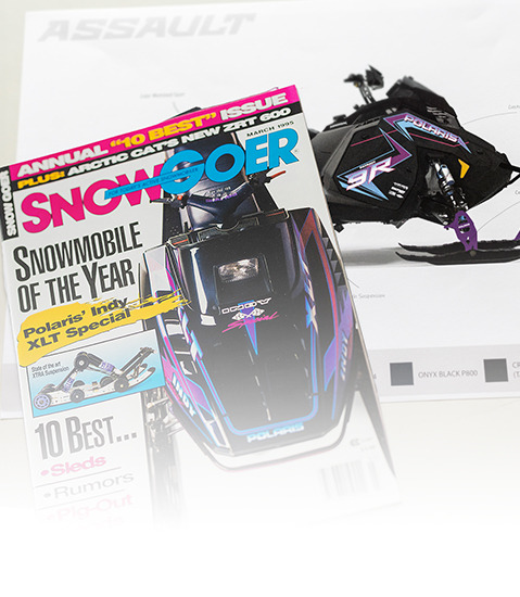 Close-up of a black Polaris snowmobile with vibrant pink, blue, and white geometric graphics on its side panel.