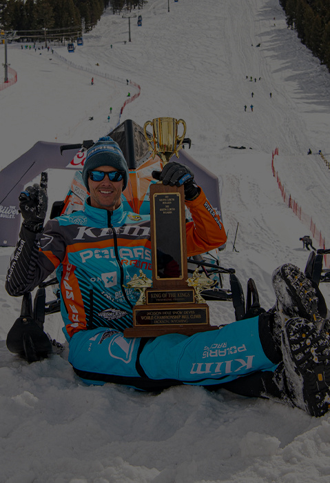 Polaris Snowmobile racers at a finish line with a trophy, flanked by branded banners and a crowd in the background.