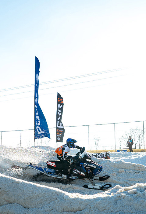 Polaris snowmobile racer speeding through a snow-covered course lined with Polaris and FXR banners.