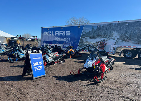 Close-up of a blue and white Polaris INDY snowmobile displayed outdoors at a SnowCheck Sneak Peek Tour event.