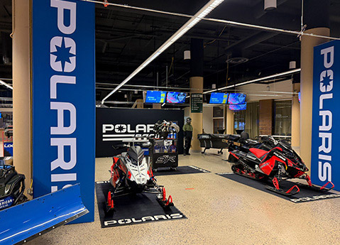 Polaris snowmobiles and riding gear displayed inside a branded event booth with blue banners and product exhibits.