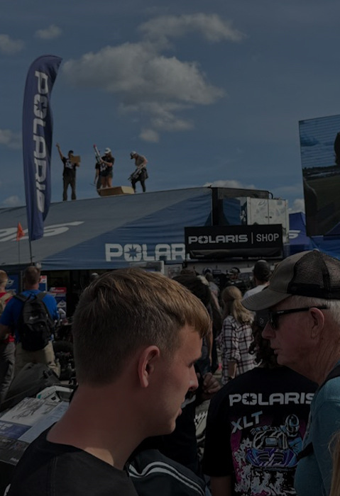 Polaris Snowmobile outdoor event with a crowd gathered around Polaris banners and a large screen displaying a person celebrating.