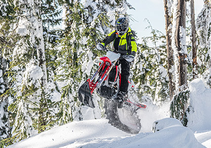 Un motoneigiste en train de faire un essai routier sur une moto sur neige Timbersled sur des bosses dans l’arrière-pays