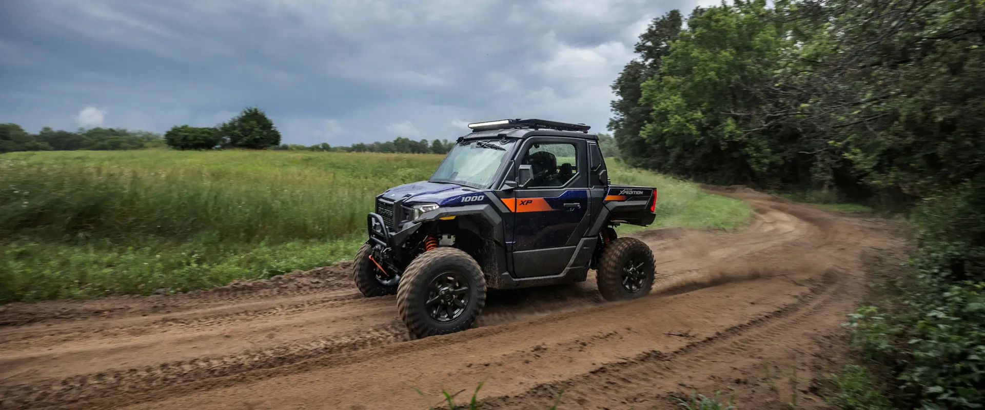 2 people on bikes riding away from a 2025 Polaris XPEDITION XP side-by-side with bike rack accessory installed.