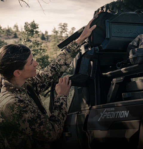 Woman grabbing gear from the adaptable cargo box on a 2025 Polaris XPEDITION XP Performance Side-by-Side.