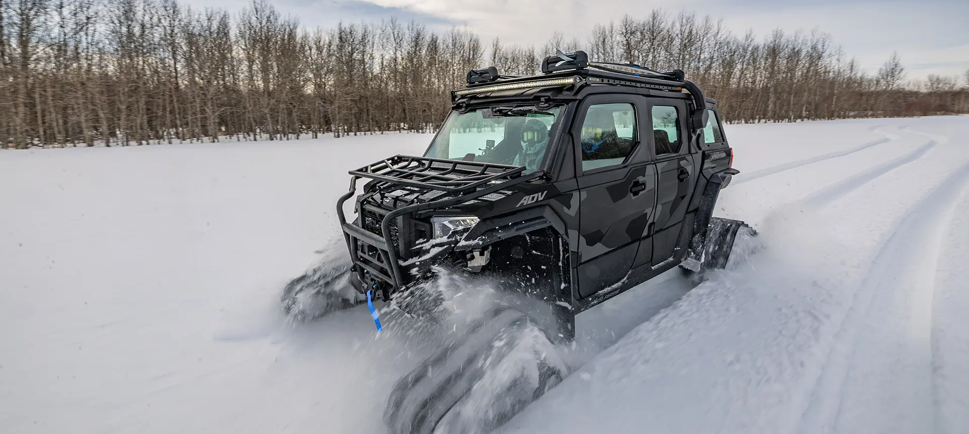 A 2026 Polaris XPEDITION ADV 5 NorthStar side-by-side with tracks installed traversing a snow-covered field.