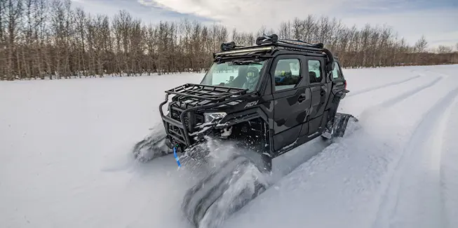 A 2026 Polaris XPEDITION ADV 5 NorthStar side-by-side with tracks installed traversing a snow-covered field.