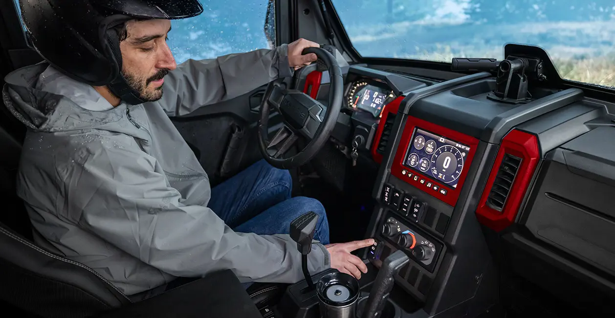 A man in a 2026 Polaris XPEDITION performance side-by-side using the windshield wiper switch.