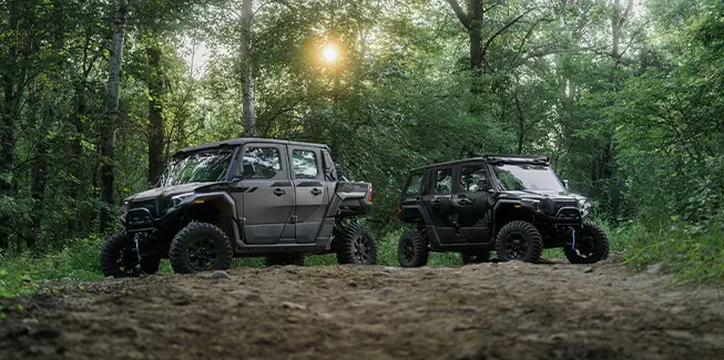A 2026 Polaris XPEDITION XP 5 NorthStar side-by-side & a 2026 Polaris XPEDITION ADV 5 NorthStar side-by-side parked in forest.