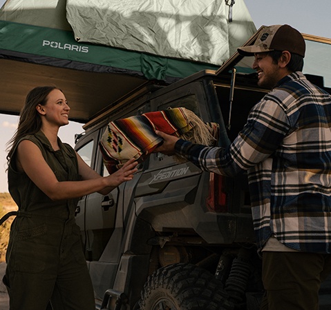 A man handing a blanket to a woman that he grabbed from the cargo box of a 2026 Polaris XPEDITION ADV 5 performance SxS.