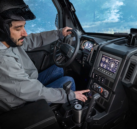 Man using the heat and AC dials while inside the all-season cab of a 2026 Polaris XPEDITION ADV SxS.