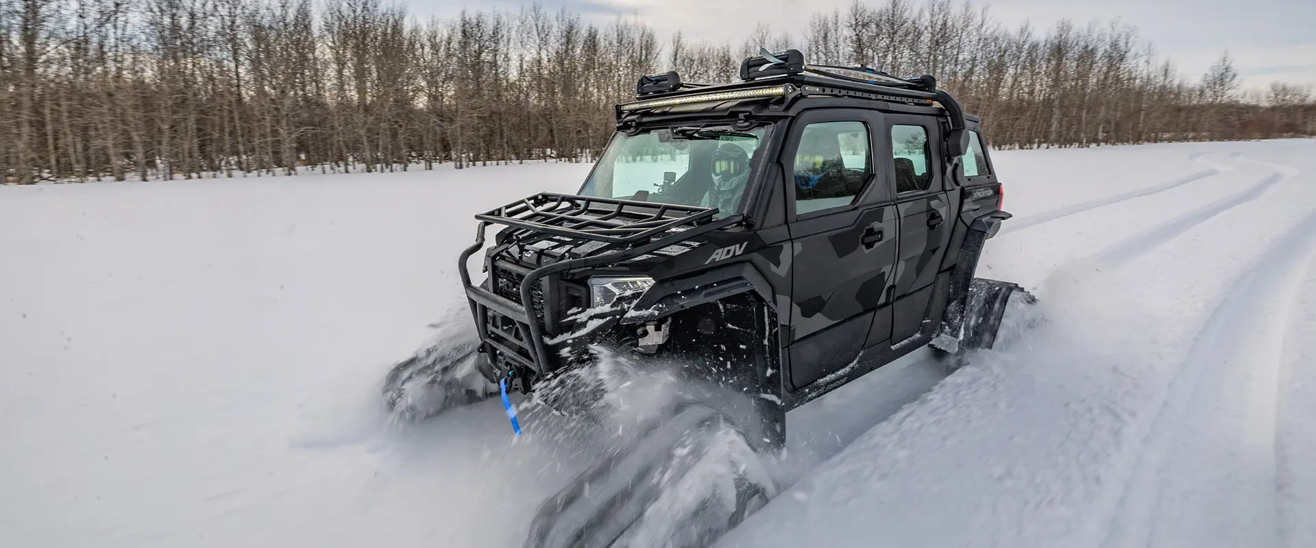 A 2026 Polaris XPEDITION ADV 5 NorthStar performance SxS with tracks installed cruising through a snowy field.