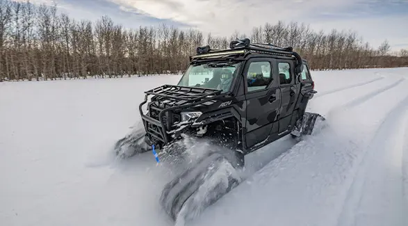 A 2026 Polaris XPEDITION ADV 5 NorthStar performance SxS with tracks installed cruising through a snowy field.