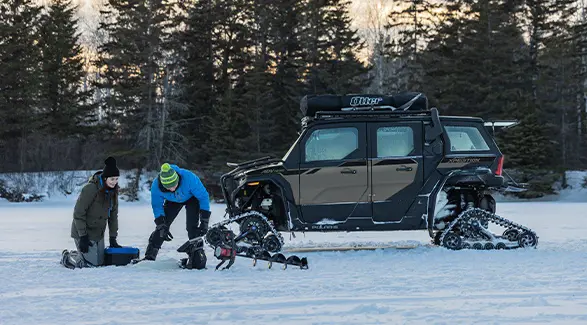 2 people ice fishing while their 2026 Polaris XPEDITION ADV NorthStar performance side-by-side with tracks is parked in the background.