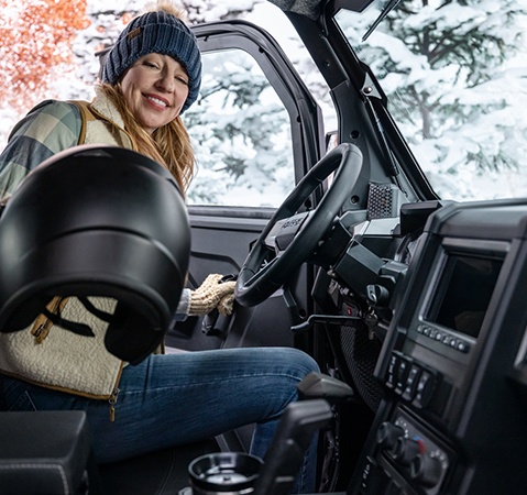 Woman grabbing a helmet while entering the factory-installed cab of a 2026 Polaris XPEDITION XP NorthStar SxS.