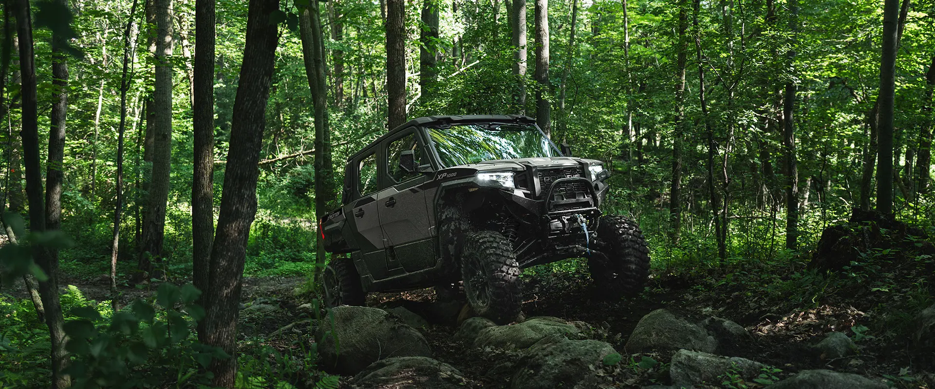 A 2026 Polaris XPEDITION XP 5 NorthStar side-by-side climbing over rocky terrain with ease in a forest.