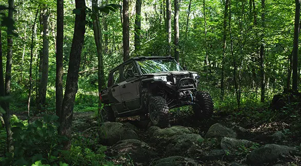A 2026 Polaris XPEDITION XP 5 NorthStar side-by-side climbing over rocky terrain with ease in a forest.