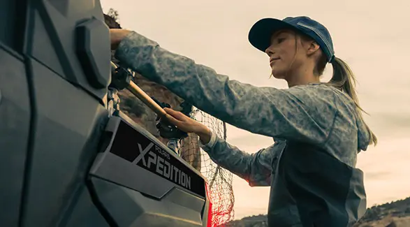 A woman putting a fishing net onto a rack installed on the cargo box of a 2026 Polaris XPEDITION XP NorthStar side-by-side.