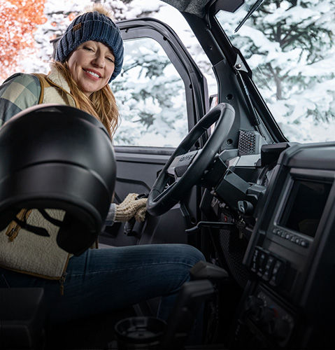 A woman grabbing a helmet as she steps into a Polaris XPEDITION enclosed cab performance side-by-side.
