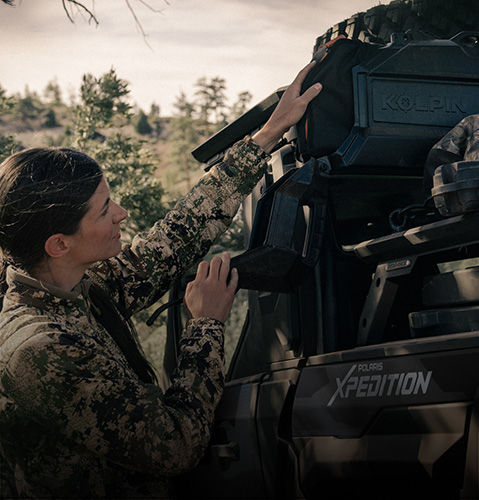 A woman grabbing gear from the cargo box of a Polaris XPEDITION performance side-by-side.