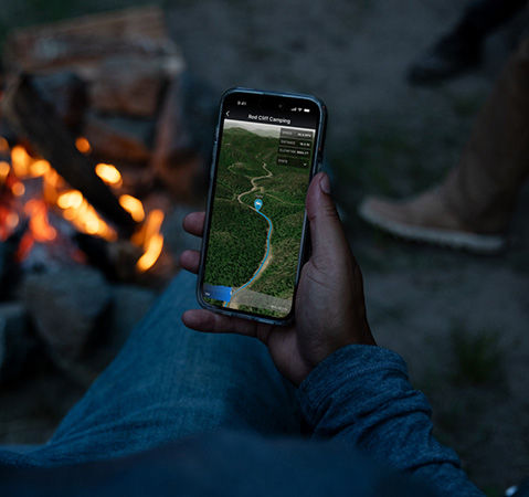 A person using the RIDE COMMAND app to share a route while sitting at a campfire.