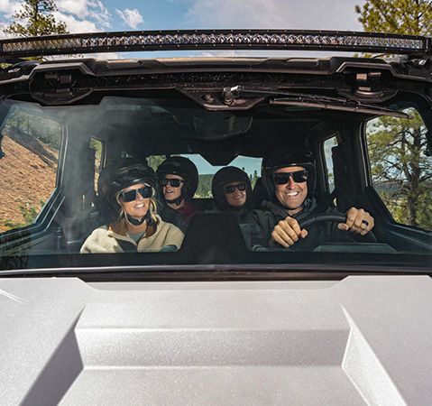 4 people enjoying the AC in the enclosed cab of a 2027 Polaris XPEDITION ADV side-by-side.