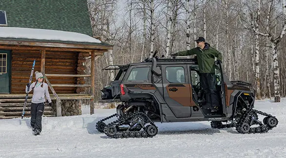 2 people gearing up to go skiing near a 2027 Polaris XPEDITION ADV 5 NorthStar side-by-side.